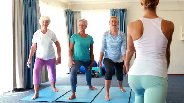 Trainer assisting senior citizens in performing stretching exercise