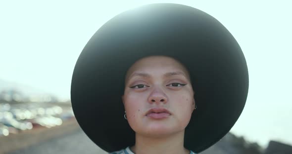 Young bald girl wearing trendy hat and looking on camera with sunset in the background