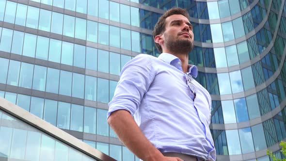 A Businessman Stands in Front of an Office Building and Looks Around Proudly - Closeup From Below