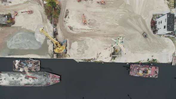 Port cargo cranes on the river bank produce sand. Tractors and excavators in industrial area  