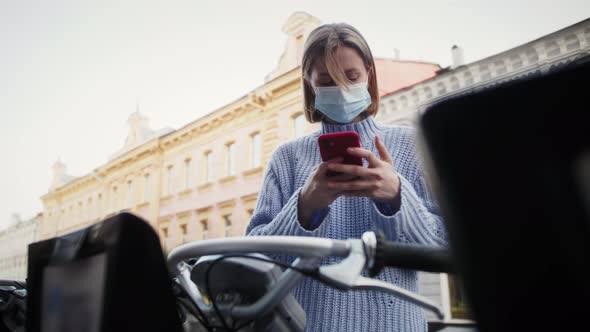 Tourist in medical mask take scooter or bike bicycle in sharing parking lot.