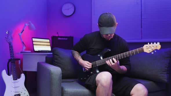 Man Plays the Electric Guitar on Sofa With Color Led Lights At Home Studio