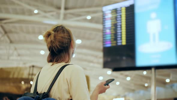 Tourist in Medical Face Mask Checking Flight Departure Gate Number at Timetable Schedule Board Using