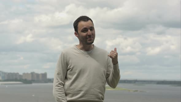 Young Expressive Man Standing Near the River, Having a Conversation and Gesturing with His Arms