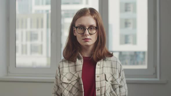 A Young Girl with Glasses Stands in an Apartment