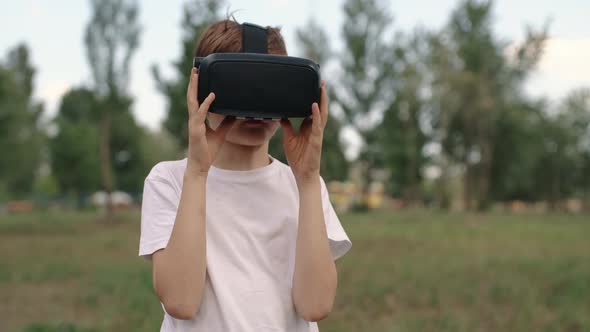 Happy Boy in Virtual Reality Glasses Plays Video Games Outdoors
