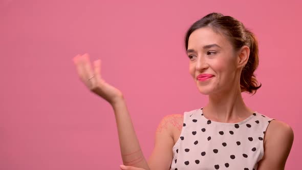 Smiling Woman Stands on a Pink Background and Shows Her Palms To the Free Space.