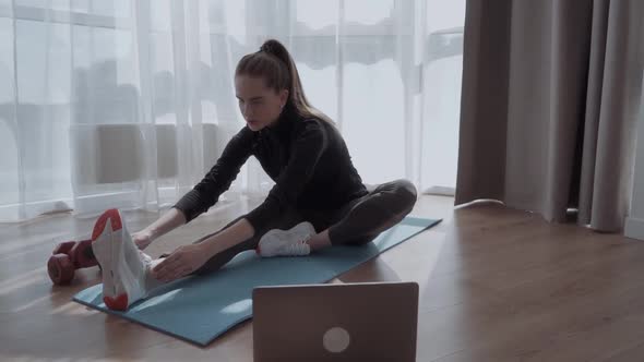 Female in Sportswear is Sitting on Floor on Mat at Home Watching a Video Instruction in a Laptop