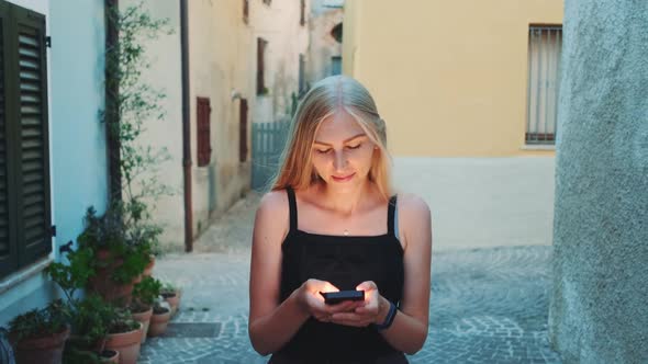 Beautiful Young Lady Chatting on Smartphone While Walking on the Street