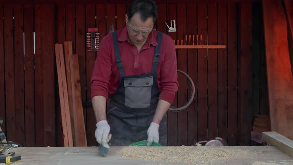 Carpenter Cleans Wooden Workbench with Brush. Cleaning Workplace After Work