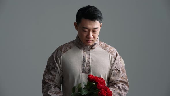 Smiling soldier Asian man holds out a bouquet of red roses to the camera