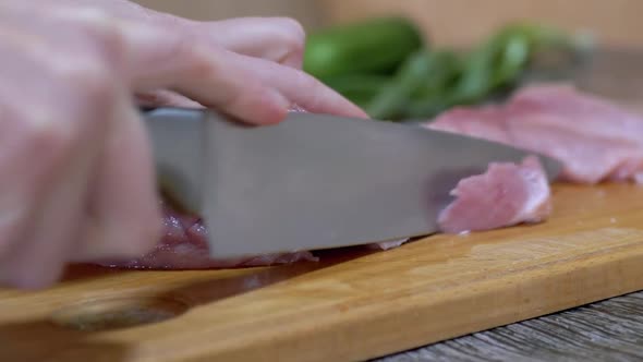 Female Hands Cuts Raw Pork Meat with a Sharp Knife on a Cutting Wood Board