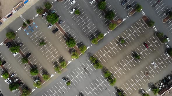 Aerial tracking downward shot of a large shopping center and its parking lot with shoppers driving.