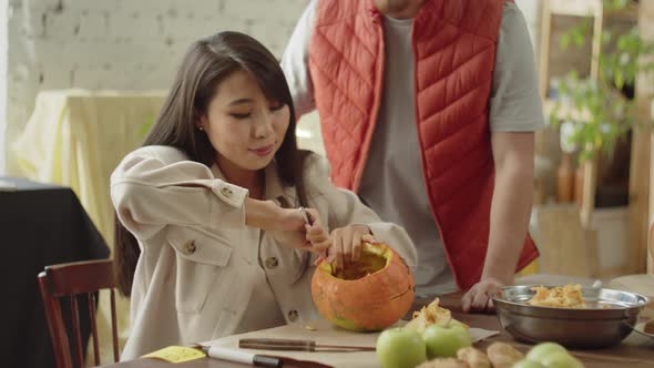 A Beautiful Young Lady is Taking the Pulp Out of the Pumpkin and a Young Man is Watching