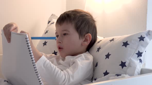 Little boy drawing in bed at home. Education talent concept.