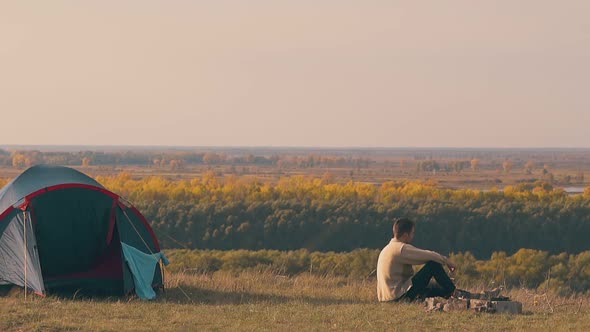 Sad Guy Sits By Camp Bonfire and Looks at Autumn Forests