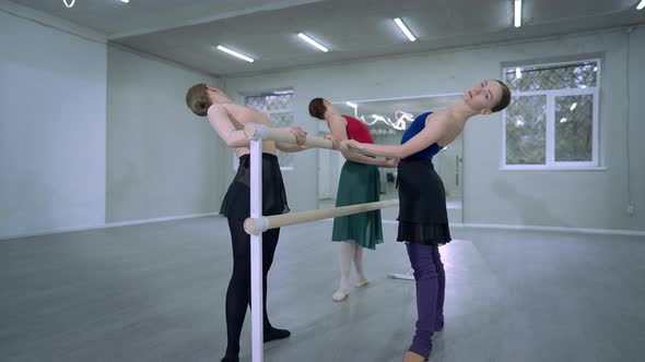 Three Flexible Slim Elegant Women Rehearsing Ballet Dance at Barre Bending Back Raising Hand