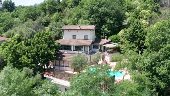 Flying up to small Mediterranean villa with pool surrounded by trees