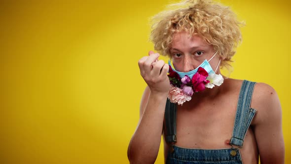 Young Caucasian Man in Covid Face Mask Squeezing Flower in Hand Posing on the Right at Yellow