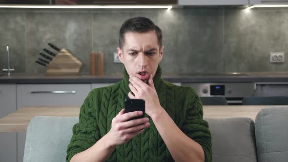 Busy Man Reading Trouble Message on His Smartphone While Sitting on the Couch at Home