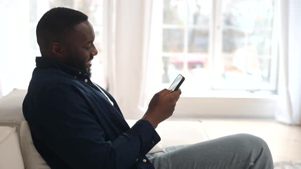 Attractive Millennial Bearded AfricanAmerican Man Relaxing and Sitting on Comfy Sofa