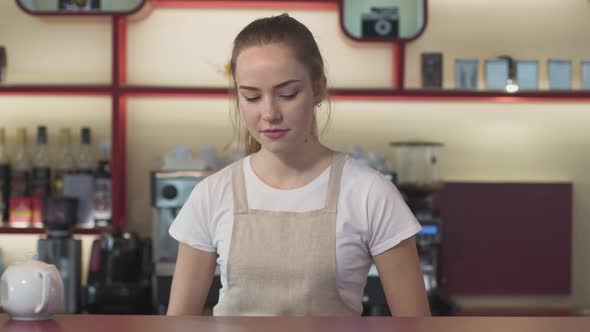 Portrait of Cheerful Young Caucasian Woman Putting Coffee Cup on the Table, Looking at Camera and