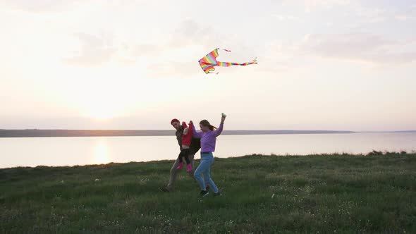 Happy Family Running with Flying Kite on Field Near Seashore During Sunset Slow Motion