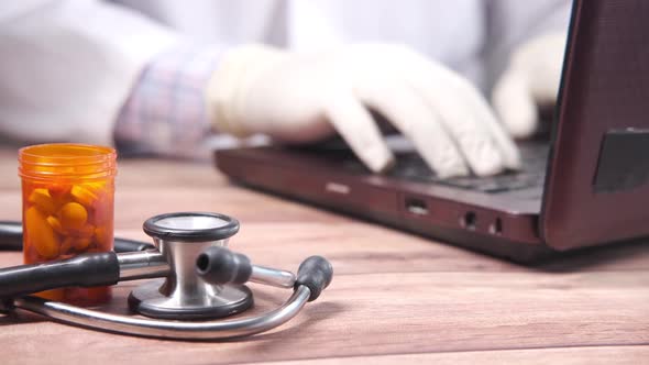 Doctor Working on Laptop with Pills Container and Stethoscope on Table