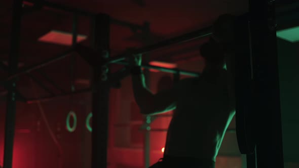 Two Men and a Woman in the Gym Do Pullups on the Horizontal Bar Together in a Dark Neon Light