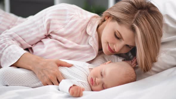 Pleasant Mother Admiring Sleeping Baby Lying on Bed Together