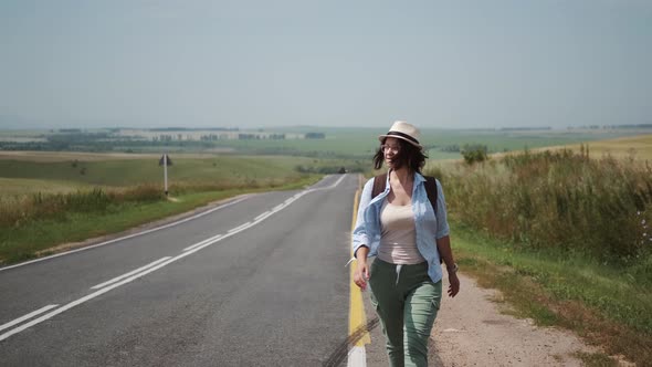 Traveler Hitchhiking By the Side of the Road. Tourist with a Backpack and a Hat Trying Stop the Car.