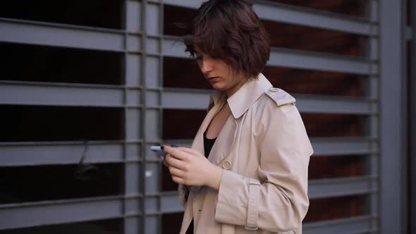 Cute Woman Chatting in Smartphone in Trench Coat