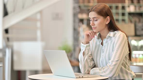 Young Latin Woman Thinking and Working on Laptop in Cafe 