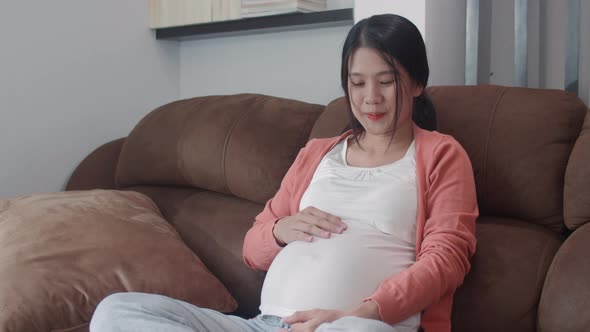 Young Asian Pregnant woman holding her belly talking with her child feeling happy smiling