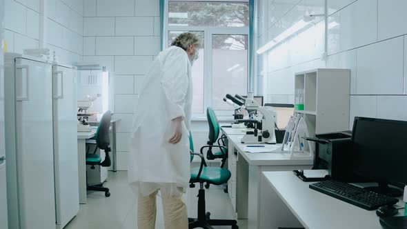 Laboratory Assistant Sits on a Chair and Works with a Microscope in White Lab