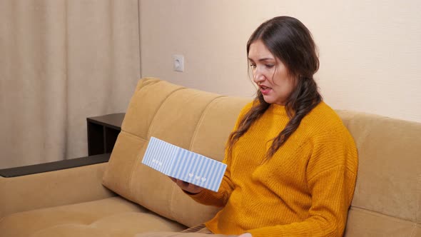 Young Woman Upset About Received Gift Sitting on Sofa