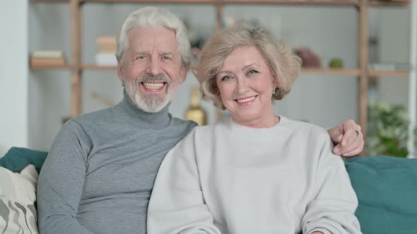Old Couple Sitting on Sofa and Smiling at Camera