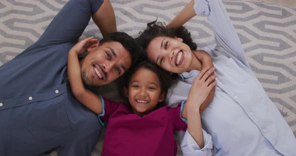 Happy hispanic parents and daughter embracing lying on floor in living room