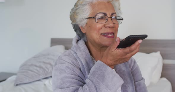 African american senior woman talking on smartphone while sitting on the bed at home