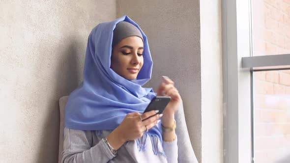 Young Attractive Muslim Woman Uses Smartphone in the Interior of Expensive Restaurant.