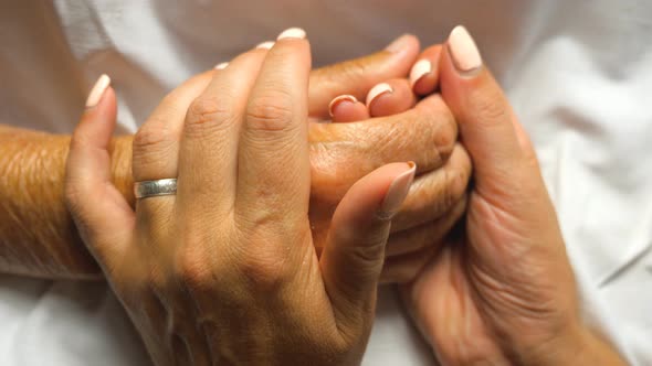Young Woman Holding and Gently Stroking Hand of Her Mother Showing Care or Love