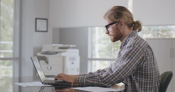 Side View of Handsome Male Entrepreneur Using Laptop Sitting at Desk in Office