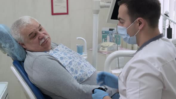 Male Dentist Consulting Elderly Patient Before Dental Treatment