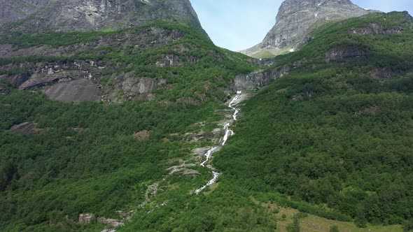 River flowing down hillside in Olden Norway - Tall mountains and lush forest with melted glacier wat