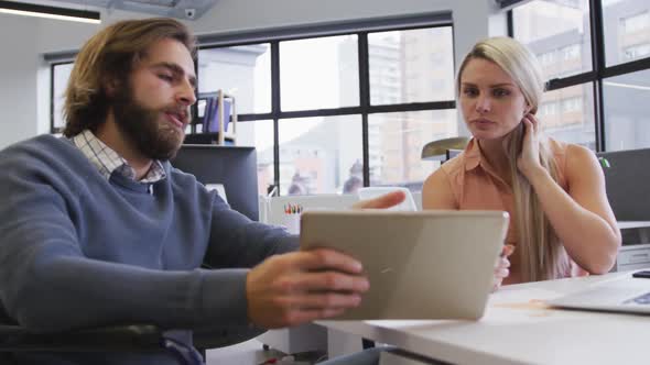 Disabled caucasian businessman sitting on wheelchair using digital tablet talking to coworker in off