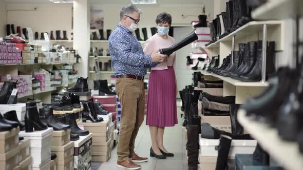 Wide Shot of Senior Caucasian Man and Woman in Covid-19 Face Masks Choosing Footwear in Shoe Store