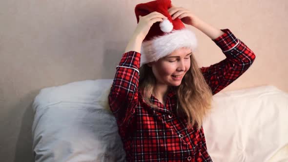 Young woman is putting on santa hat sitting in bed