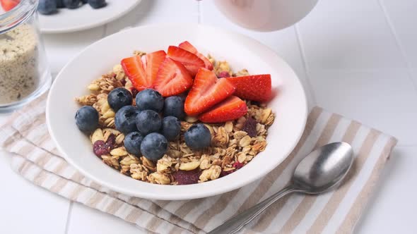 Slow motion pour milk into plate with granola and berries.