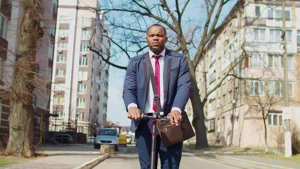 Pleasant African Male Entrepreneur Driving Electric Scooter in City