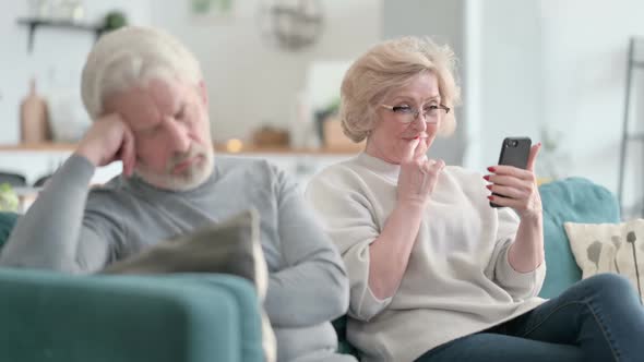 Beautiful Old Woman Using Smartphone While Old Man Taking Nap on Sofa
